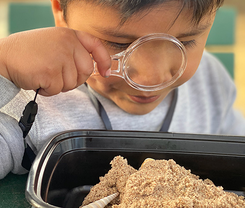 A child looking at sand through a magnifying glass
