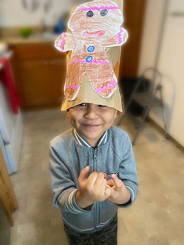 A child wearing a paper hat with a hand-drawn gingerbread man.